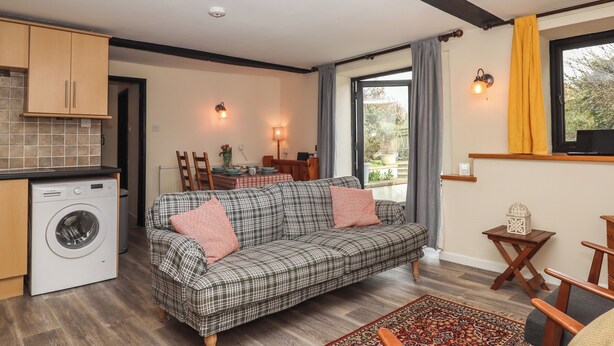 A compact living space with a sofa, a dining table, a washing machine, and a window with curtains.