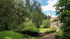 A stone building with a red-tiled roof, surrounded by lush greenery and a grassy area. - New Hall (Wrexham)