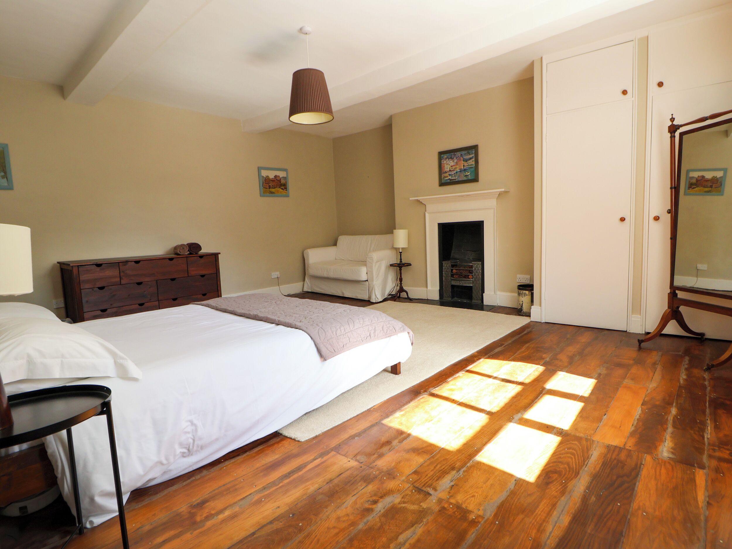 A bedroom with a large bed, a dresser, a chair, a fireplace, and a mirror.
