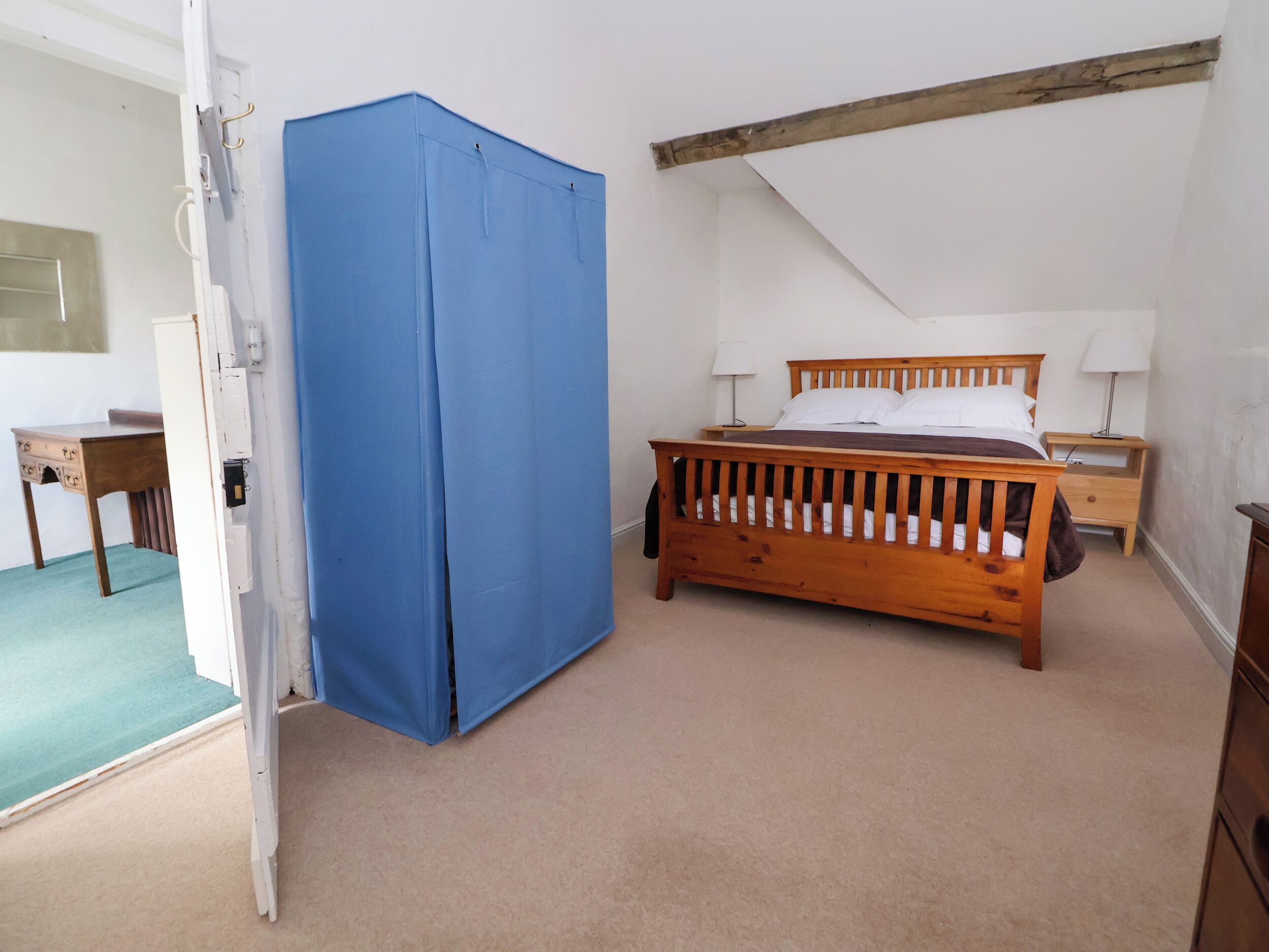 A bedroom with a wooden bed, a nightstand, a lamp, and a blue curtain.