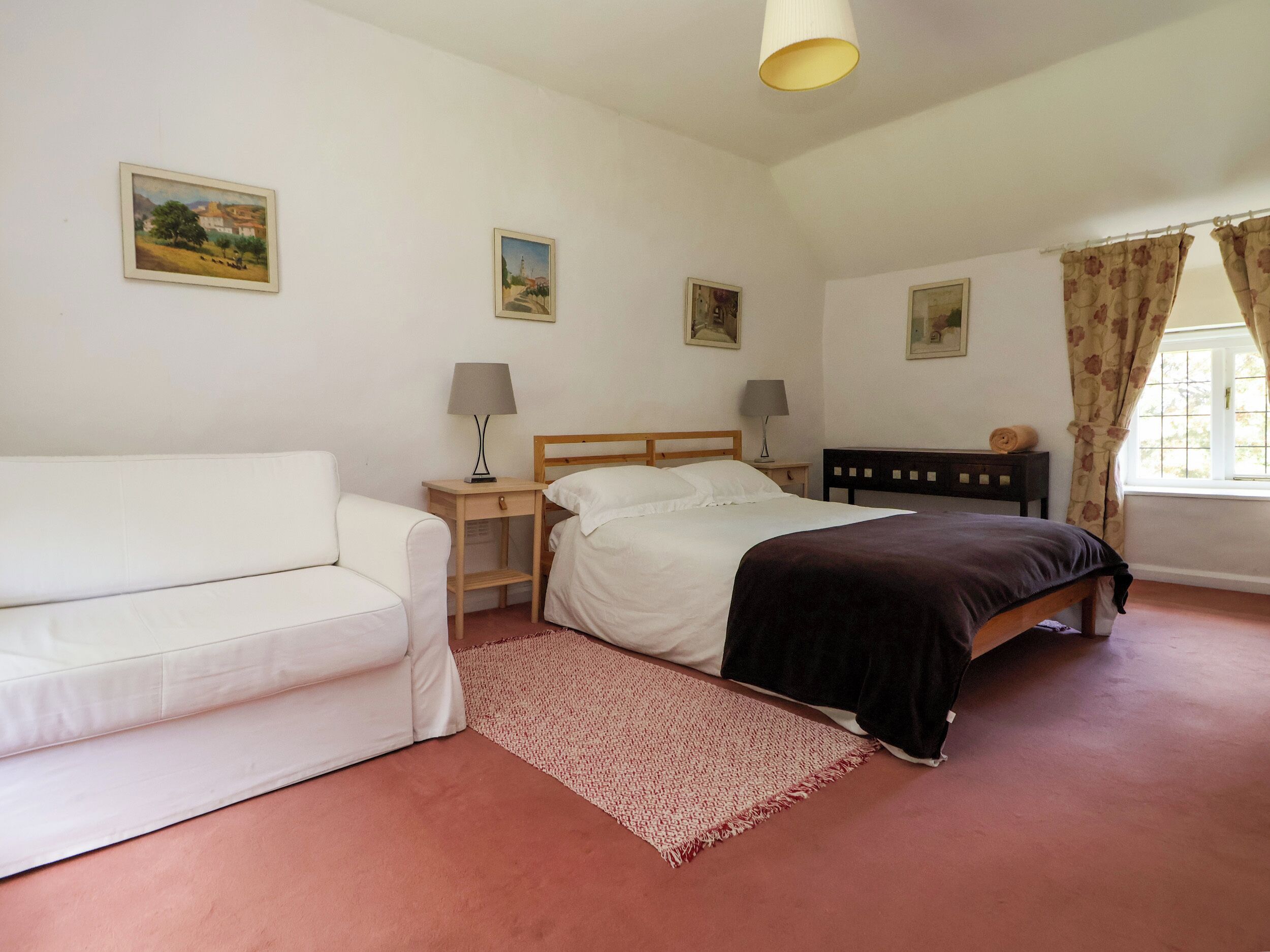 A bedroom with a bed, a bedside table with a lamp, a nightstand, a chair, and a window with curtains.