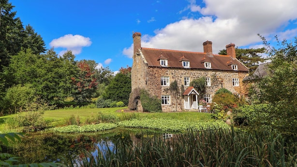 A stone building with a pond in front, surrounded by lush greenery. - New Hall (Wrexham)