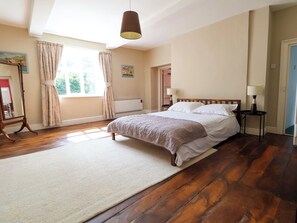 A bedroom with a large bed, wooden flooring, a standing lamp, and a window with curtains.