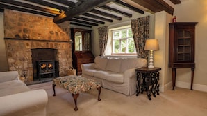 A cozy living room with a stone fireplace, a white sofa, a patterned ottoman, and a wooden cabinet. - New Hall (Wrexham)
