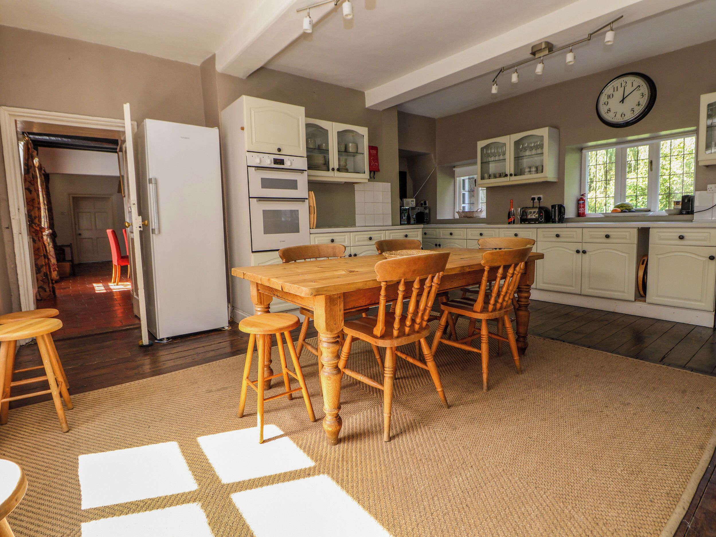 A kitchen with a wooden table and chairs, white cabinets, and a clock on the wall.