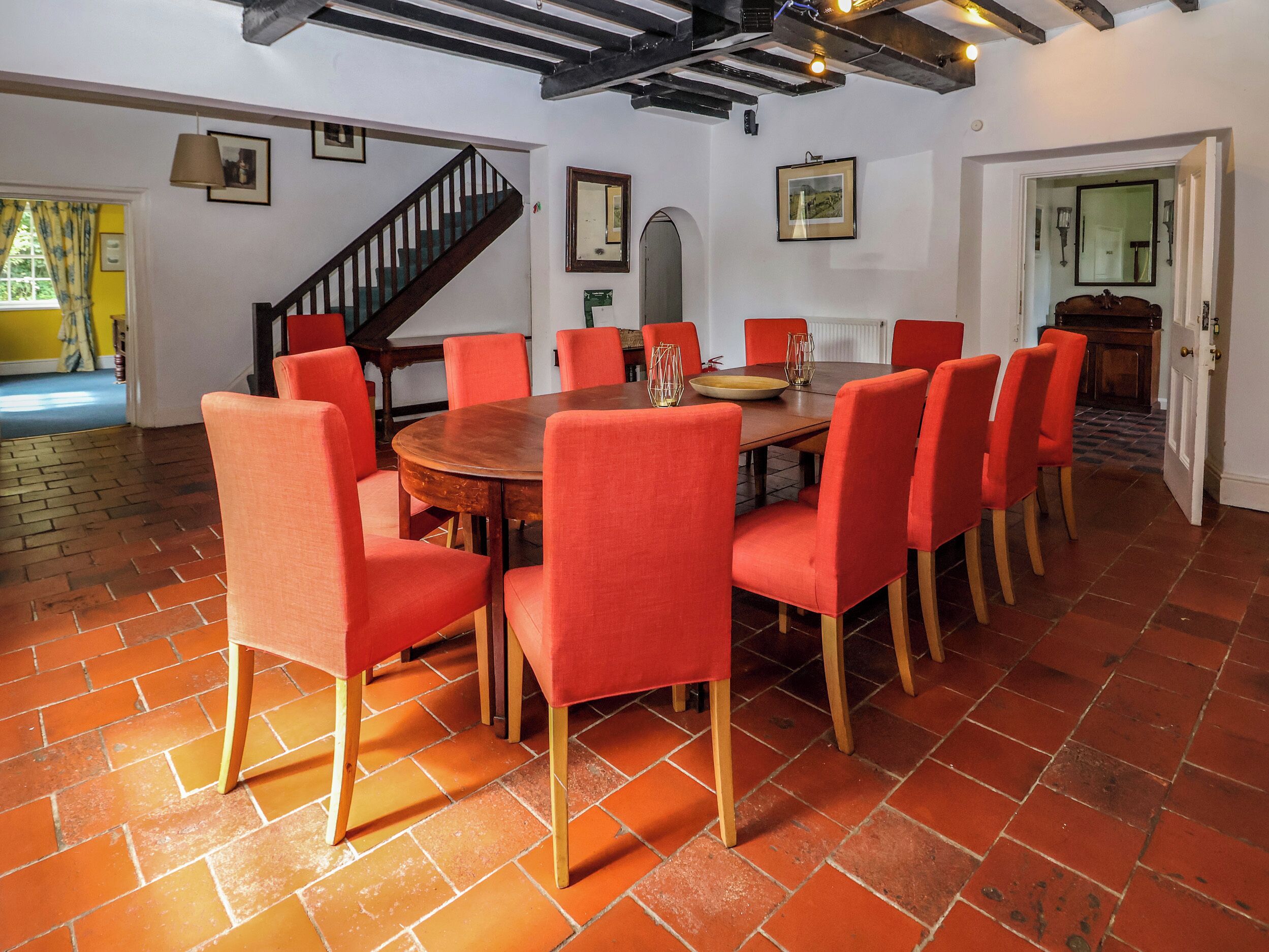 Un comedor con una mesa redonda de madera rodeada de sillas rojas, una escalera y vistas al exterior.