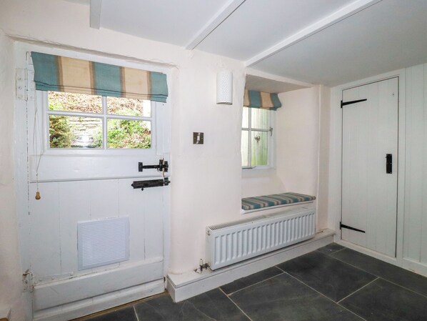 Une pièce avec une porte blanche, une fenêtre avec un store à rayures, un radiateur, un banc et une armoire.