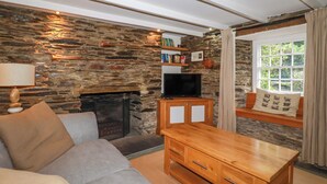 A cozy living room with a stone wall, a fireplace, a television, and a sofa. - Willow View (Wadebridge)