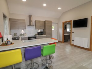 Een moderne keuken met een centraal eiland, barkrukken en een aan de muur bevestigde televisie.