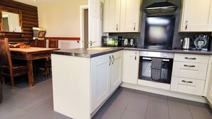 A modern kitchen with white cabinetry, a central island, and a built-in oven. - The Roe (Saint Asaph)