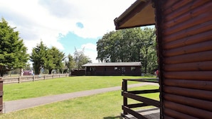 A wooden cabin with a porch, surrounded by a grassy area and trees. - The Roe (Saint Asaph)