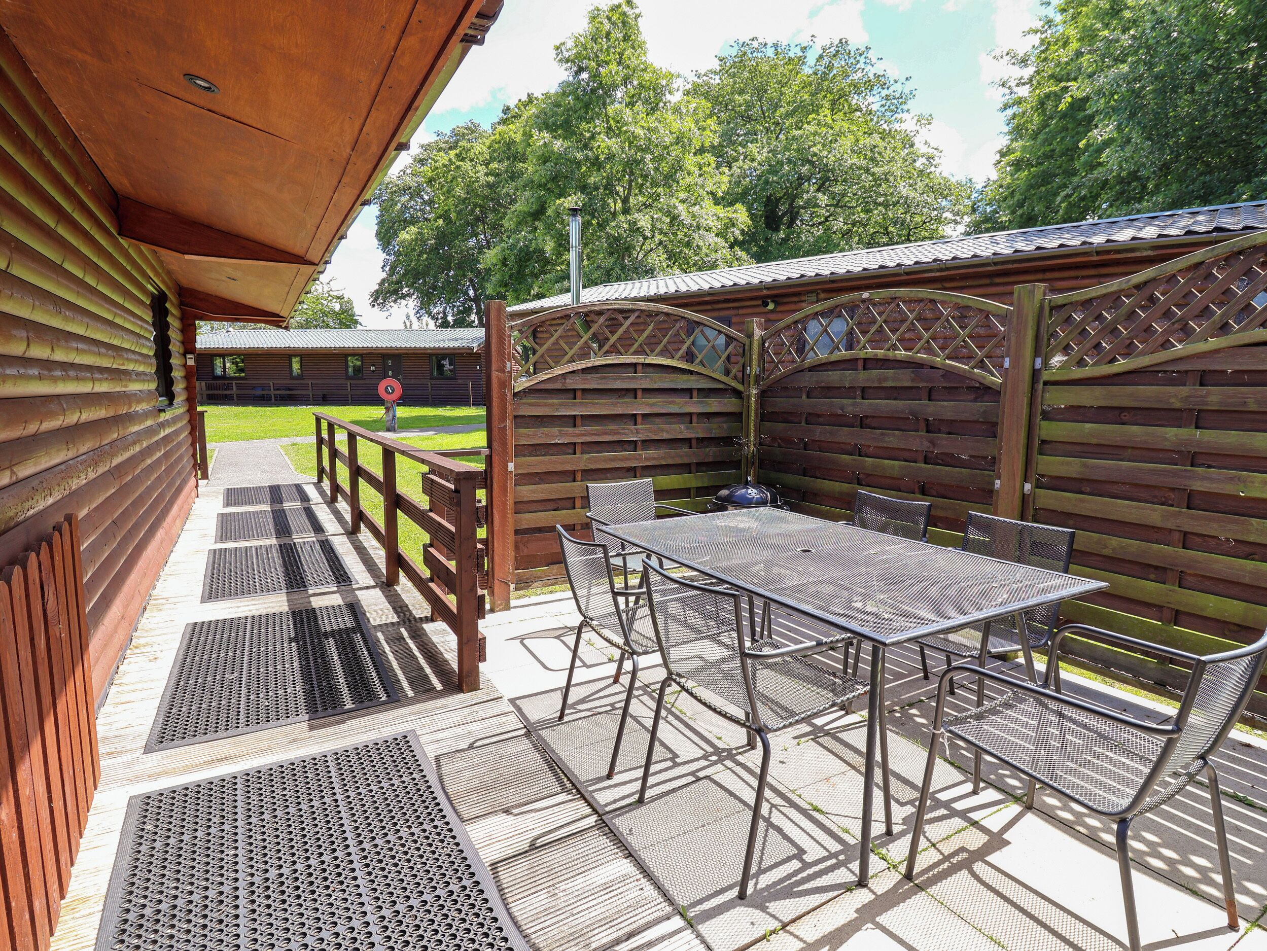 A covered outdoor patio with a table and chairs, a wooden fence, and a view of a building in the background.