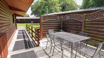 A covered outdoor patio with a table and chairs, a wooden fence, and a view of a building in the background.