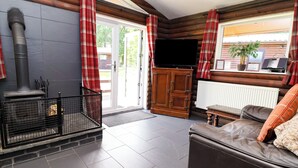 A log cabin interior with a fireplace, a sofa, a television, and a wooden cabinet. - The Roe (Saint Asaph)