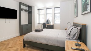 A modern bedroom with a bed, a desk, and a TV. - Park View (Llandudno)