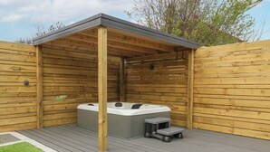 A wooden hot tub with a bench and a small table, surrounded by a wooden deck and a wooden fence. - Park View (Llandudno)