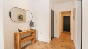 A hallway with a wooden console table, a mirror, and a door leading to another room. - Park View (Llandudno)
