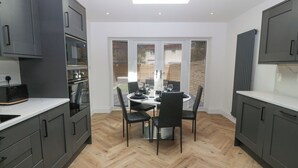 A modern kitchen with dark cabinets, a herringbone wood floor, and a skylight above the dining area. - Park View (Llandudno)
