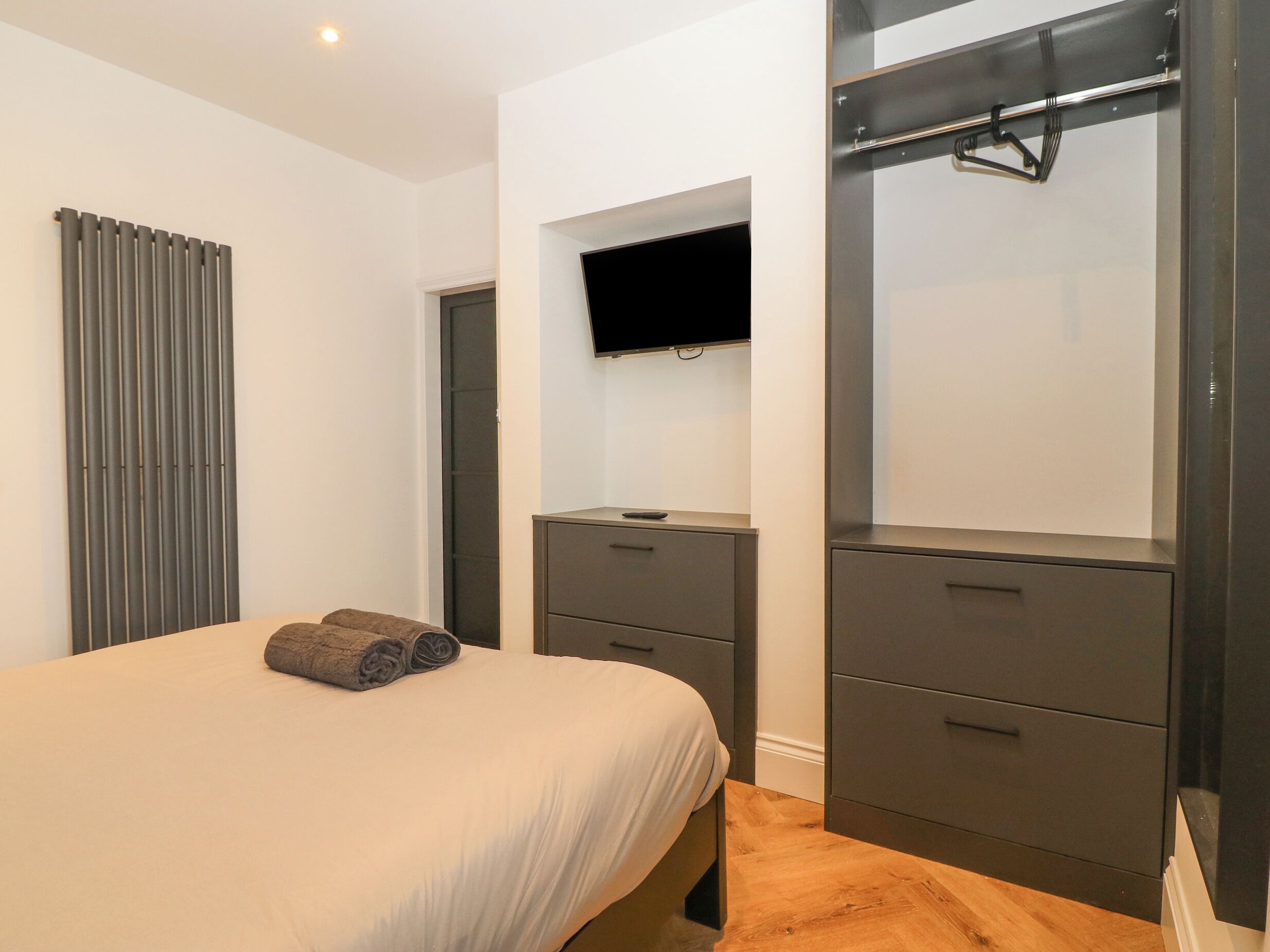 A bedroom with a bed, a TV mounted on the wall, a wardrobe, and a mirror.