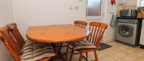 A dining area with a wooden table and chairs, a clock on the wall, a washing machine, and a kitchen area.