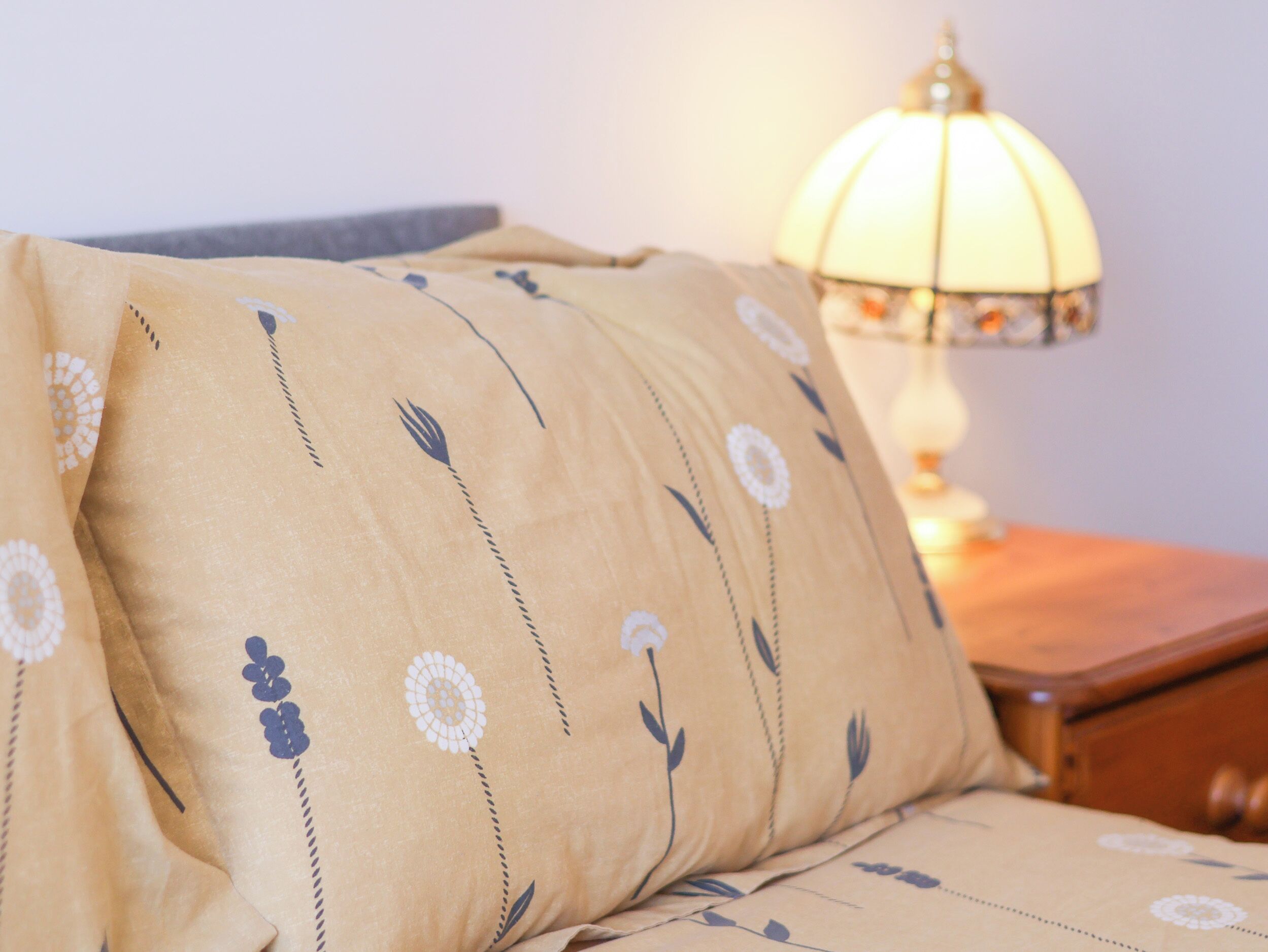A bed with a floral patterned pillow and a bedside lamp.