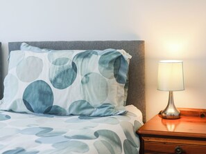 Una cama con un almohadón de diseño circular, una lámpara de noche y una mesita de madera.