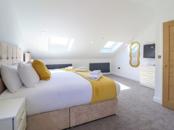 A bedroom with a large bed, a skylight, a radiator, a TV, and a wooden door. - Blackrock Gem (Porthmadog)