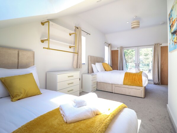 Un dormitorio moderno con dos camas, un tocador blanco y un ventanal con cortinas.