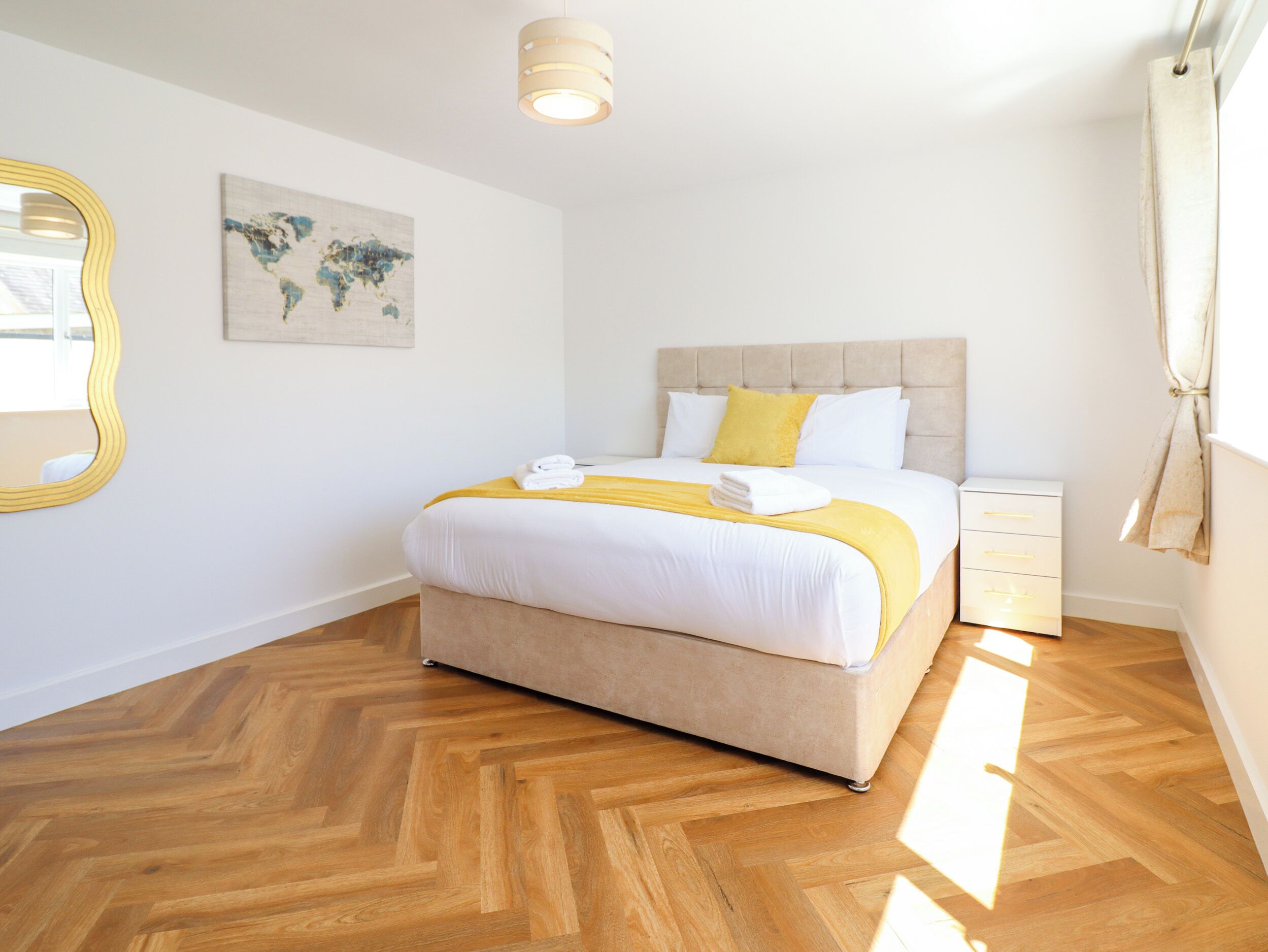 Un dormitorio ordenado con cama, mesita de noche, espejo y un mapa del mundo en la pared.
