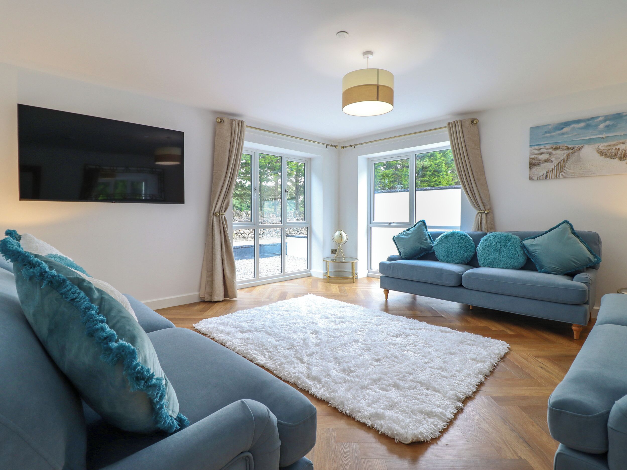 A modern living room with a grey sofa, a white fluffy rug, and a blue sofa with teal cushions.