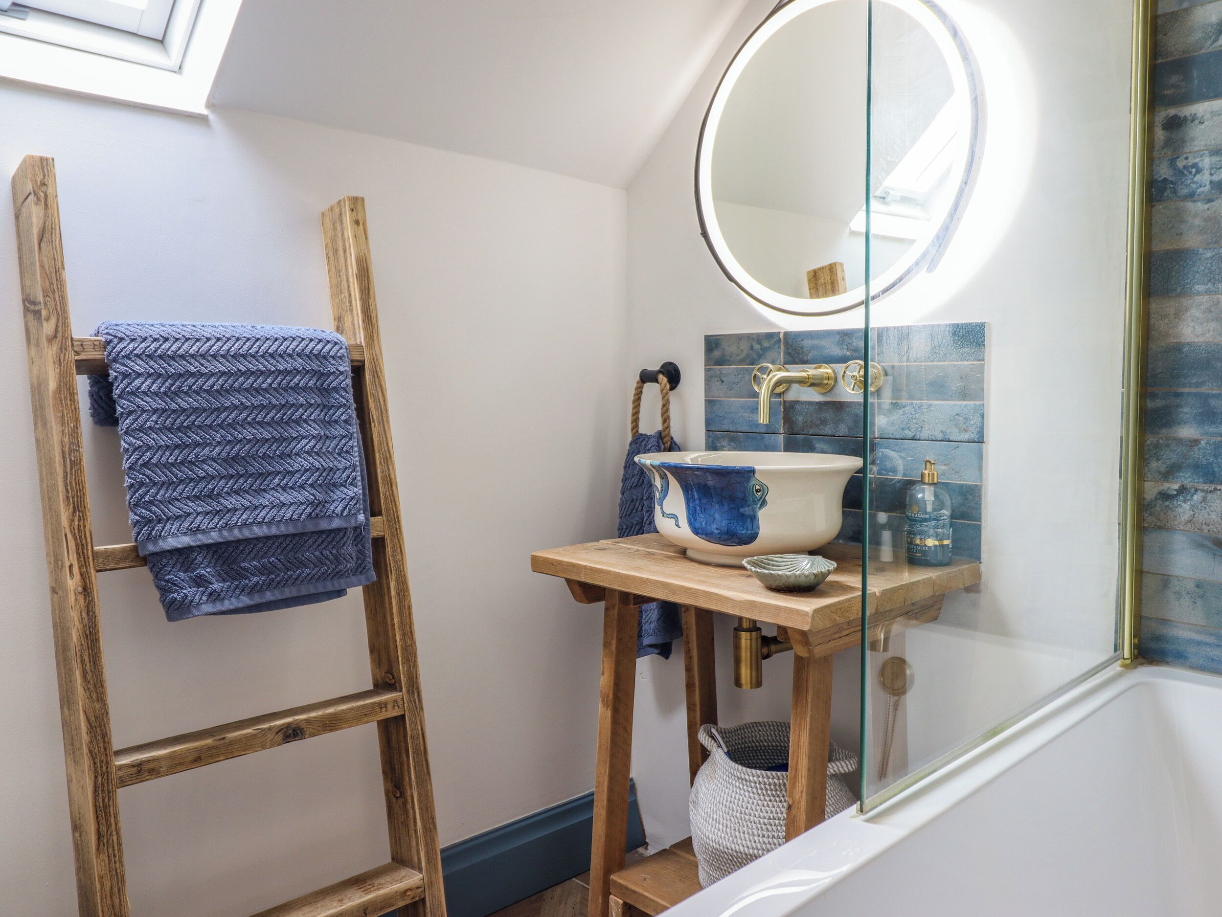 A bathroom with a wooden ladder, a blue towel, a sink with a blue vase, and a mirror.