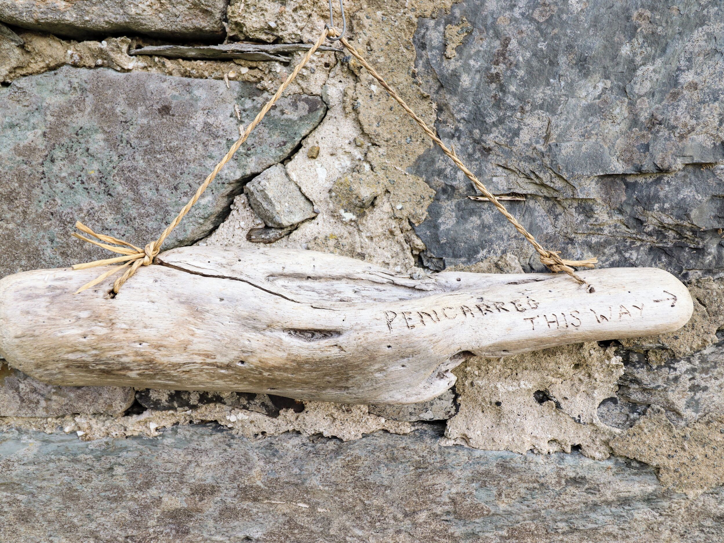 A wooden sign with the inscription "PENICARRETO THIS WAY" attached to a stone wall.