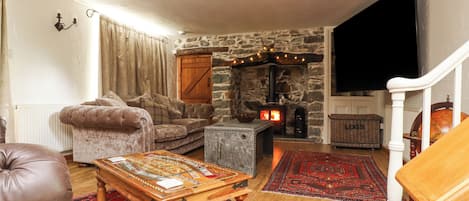 Una sala de estar acogedora con chimenea de piedra, un sofá cómodo, una mesa de centro de madera y un tapete grande.