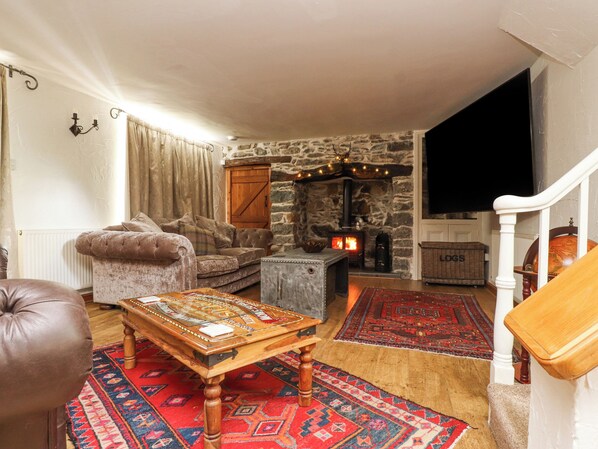 A cozy living room with a stone fireplace, a plush sofa, a wooden coffee table, and a large rug. - Ty'n Pwll Farm (Pwllheli)