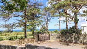 Un mur de pierre avec un portail en métal, une zone pavée et une vue sur la mer.