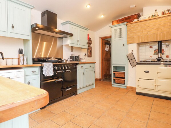 A kitchen with light blue cabinets, a black stove, and a white refrigerator. - Ty'n Pwll Farm (Pwllheli)