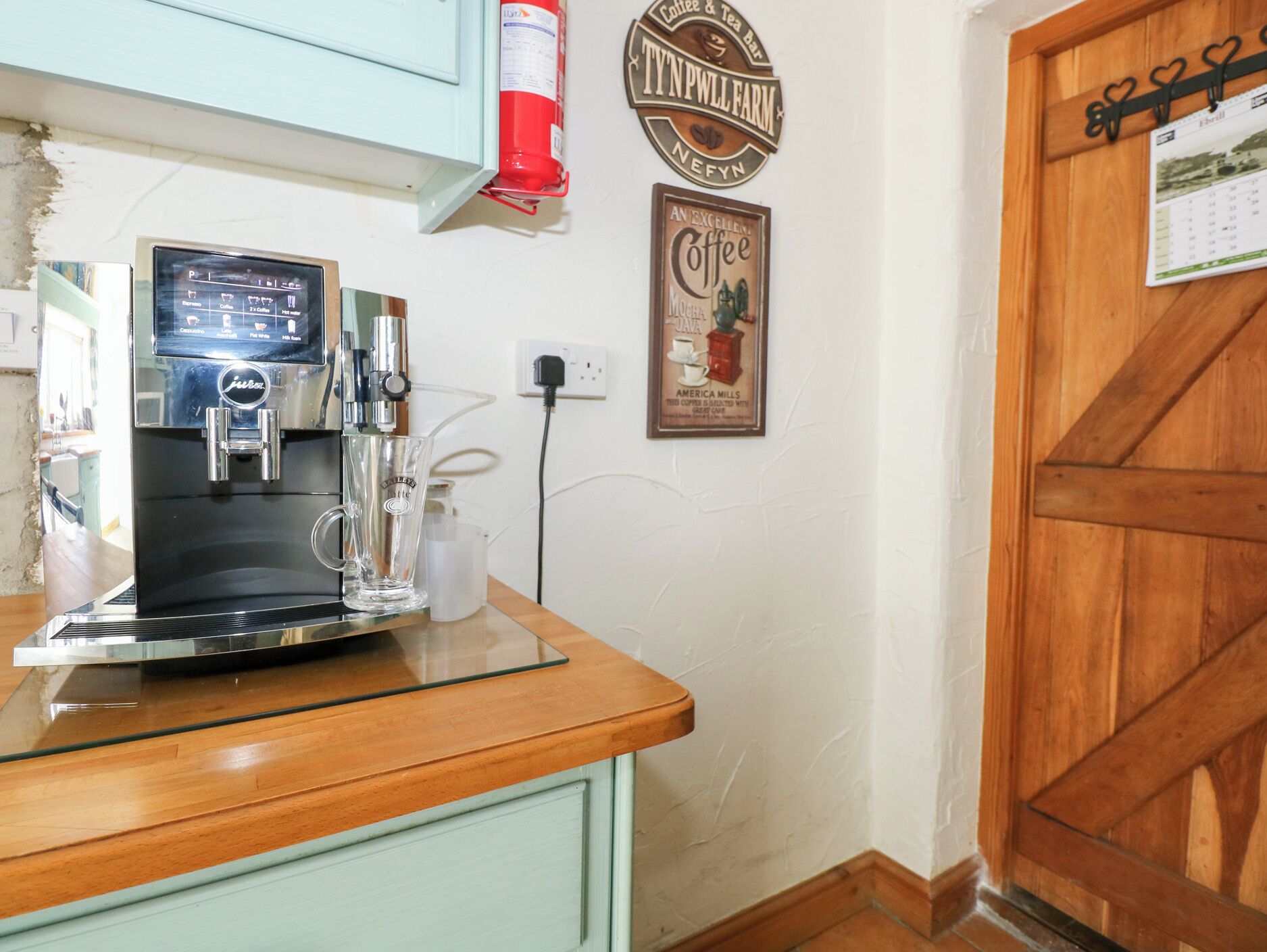 A coffee machine on a counter with a coffee mug, a fire extinguisher, and a coffee-themed sign on the wall.