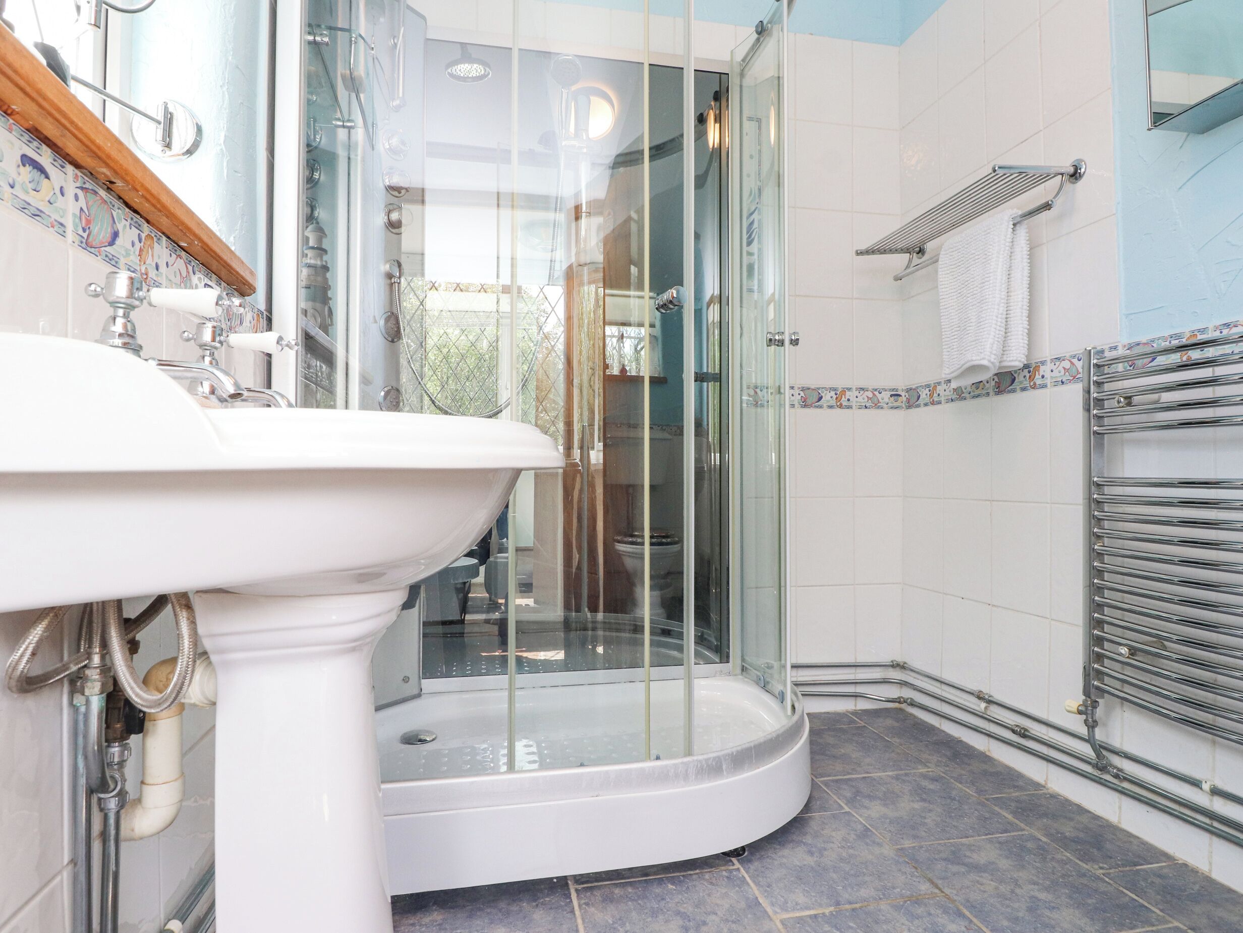 A bathroom with a glass-enclosed shower, a white sink, and tiled walls.