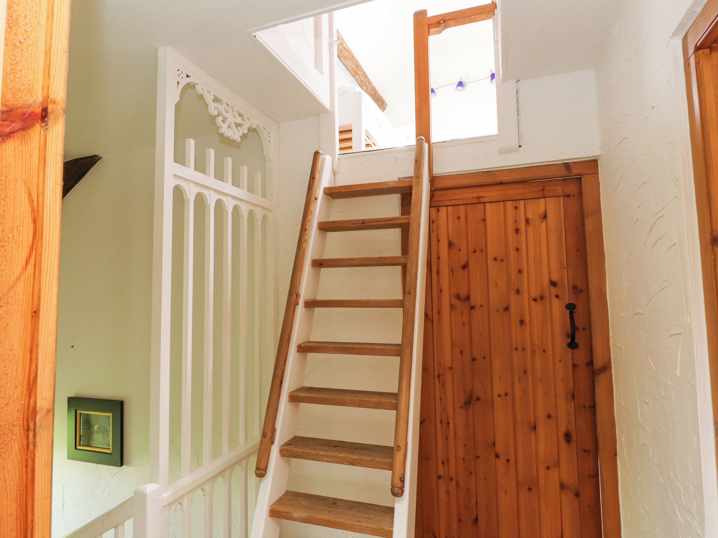 A wooden staircase with a white railing leading to a lofted area with a skylight.