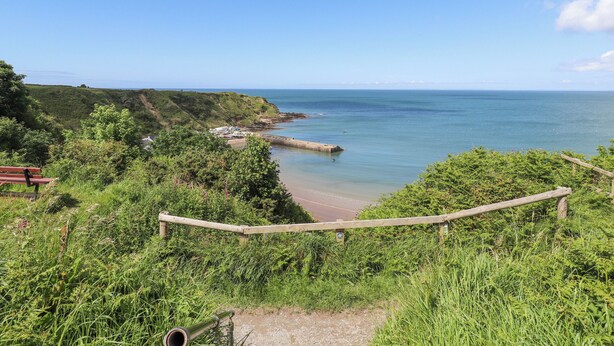 Une vue sur la côte, avec une promenade en bois, de la végétation et un ciel dégagé.