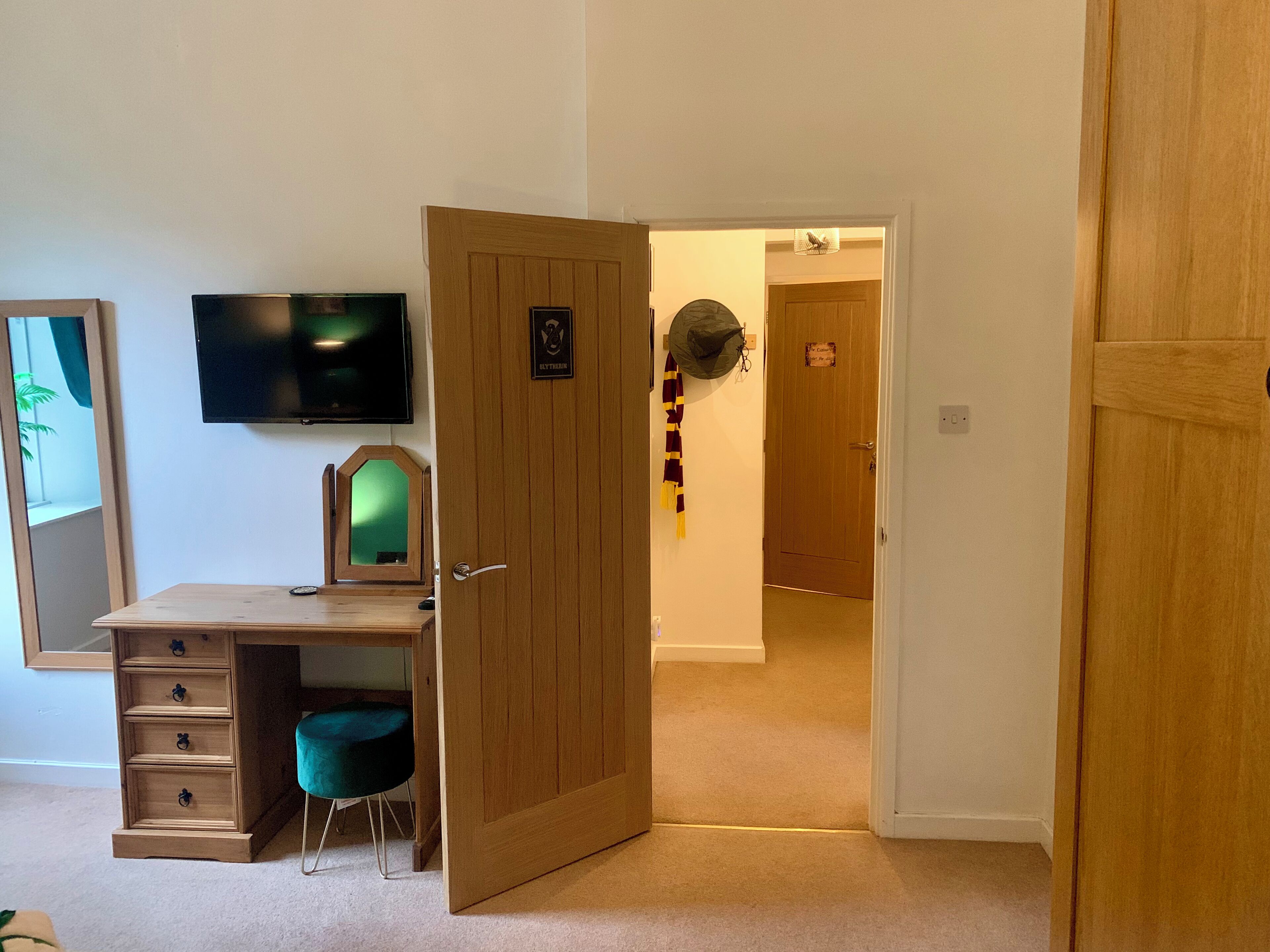 Une pièce comprenant un bureau en bois, une chaise, un téléviseur et une porte donnant sur une autre pièce.