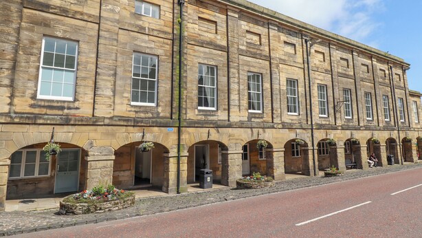 A historic stone building with multiple windows and arched doorways, likely a public building or hotel. - The Wizard's Chamber (Alnwick)