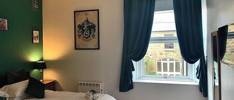 A neatly arranged bedroom with a bed, a radiator, a window with curtains, and a framed picture on the wall.