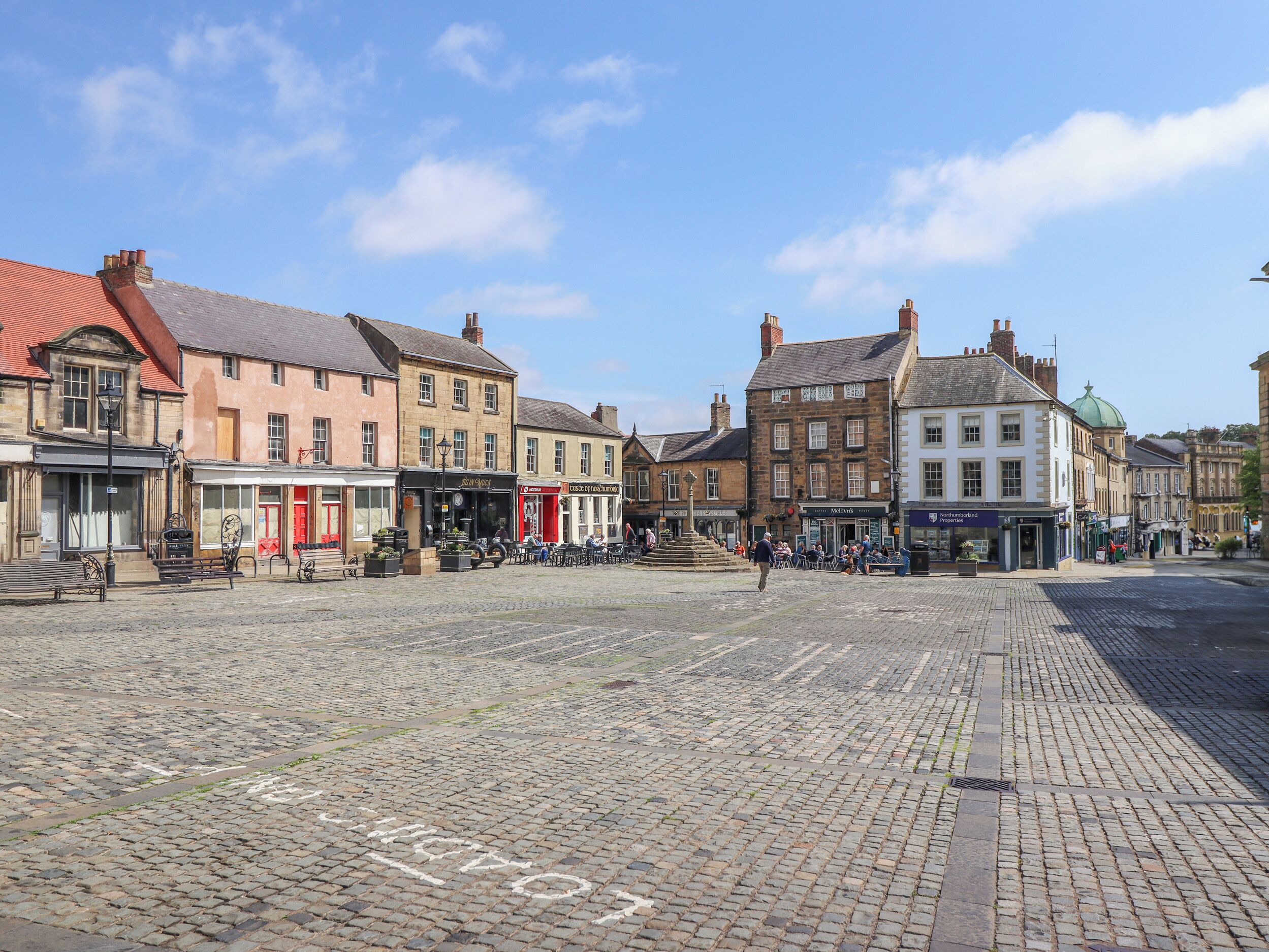 A cobblestone square with historic buildings, benches, and outdoor seating areas.