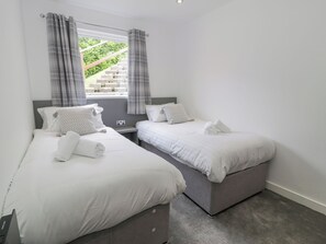 A bedroom with two beds, grey headboards, white bedding, and a window with curtains. - Luxury Lodge 62 (Rhyl)