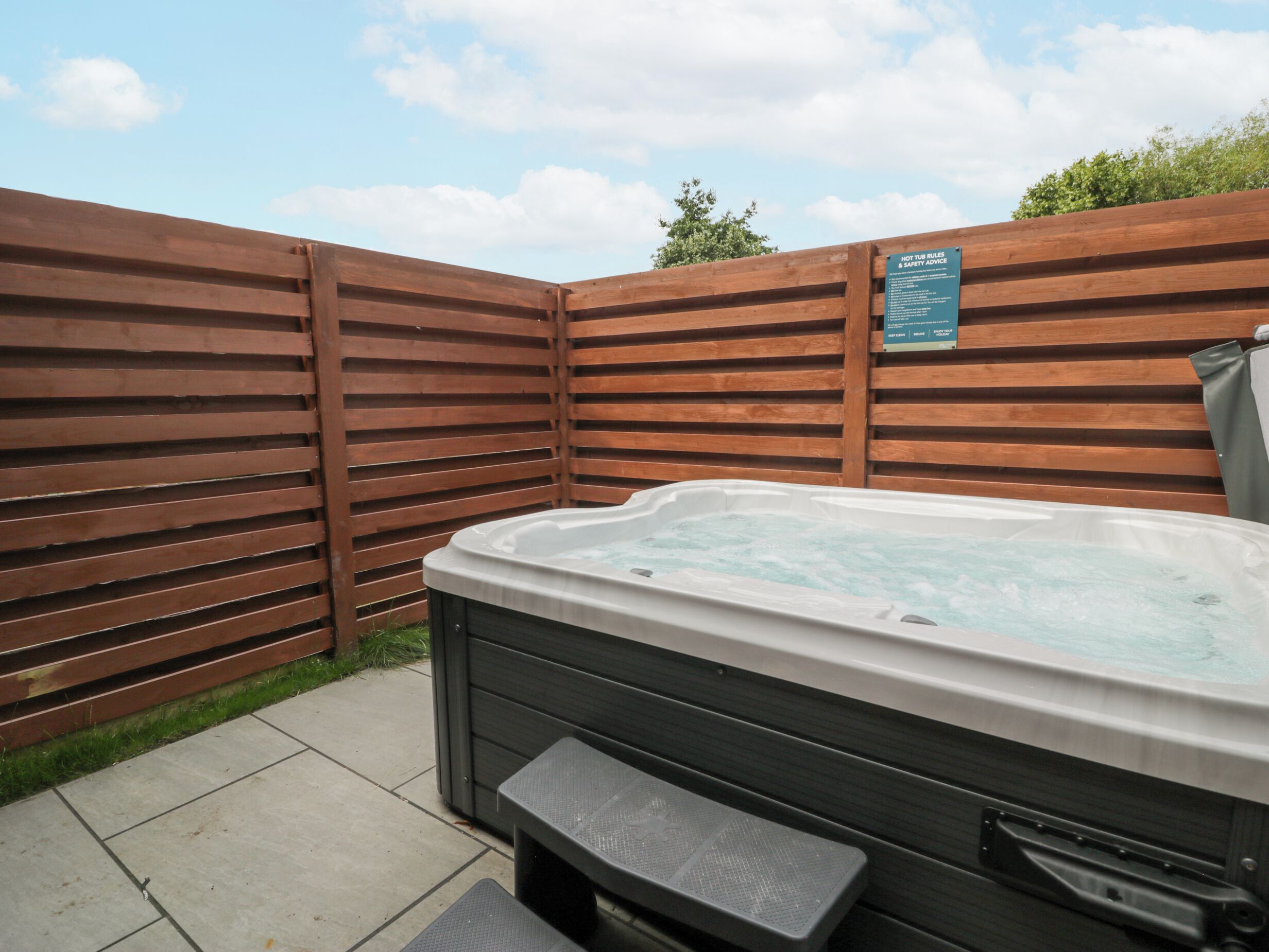 A hot tub with a wooden fence and a safety sign.
