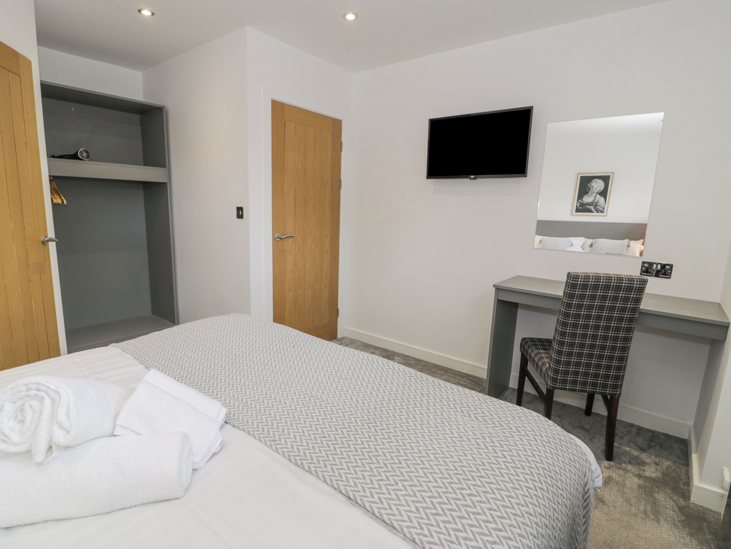Una camera d'albergo con un letto, una scrivania, una sedia, una televisione e un armadio.