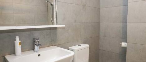 Een moderne badkamer met een witte wasbak, toilet en douche.