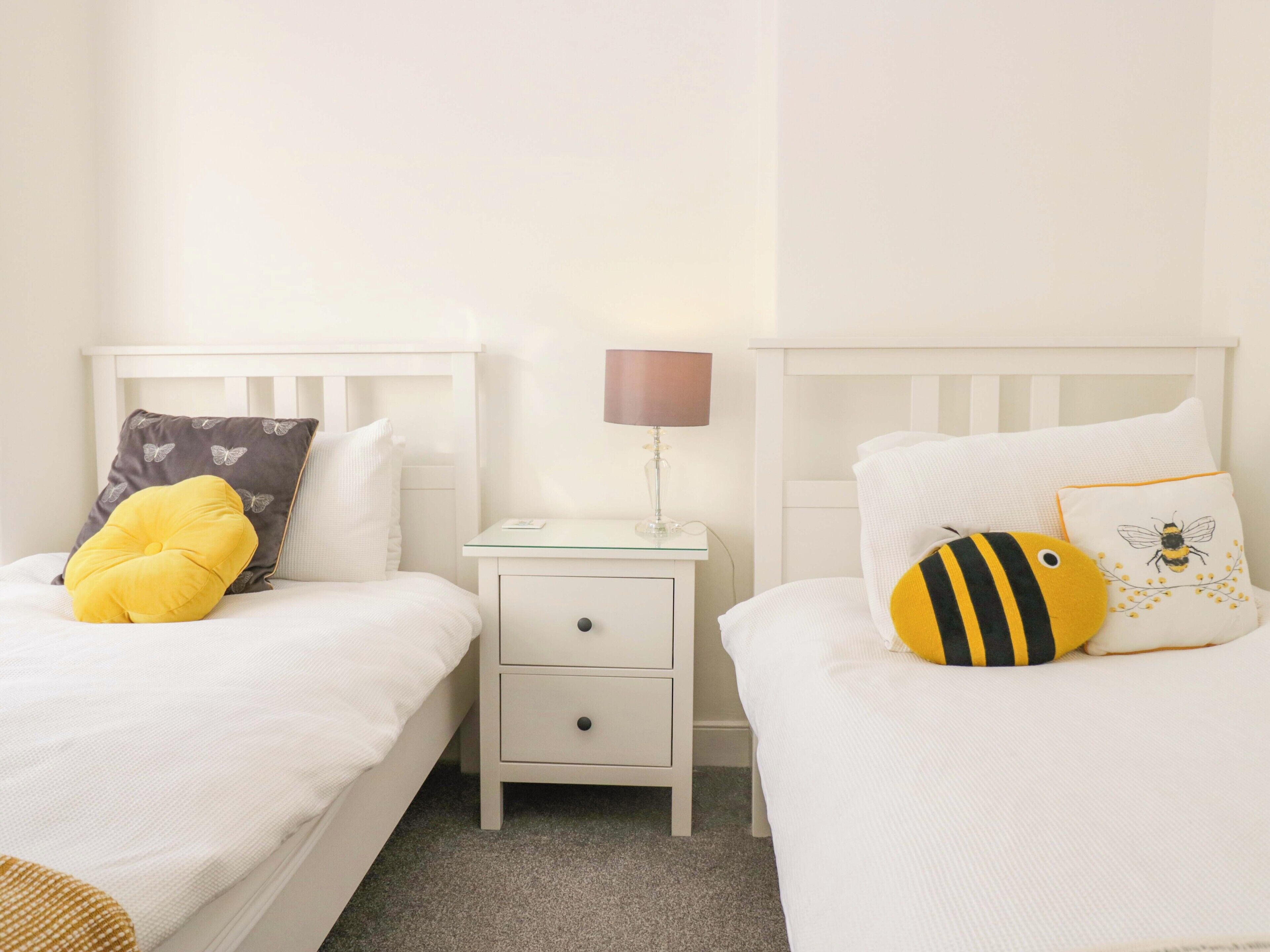 A twin room with two beds, each with a pillow and a bedside table with a lamp.