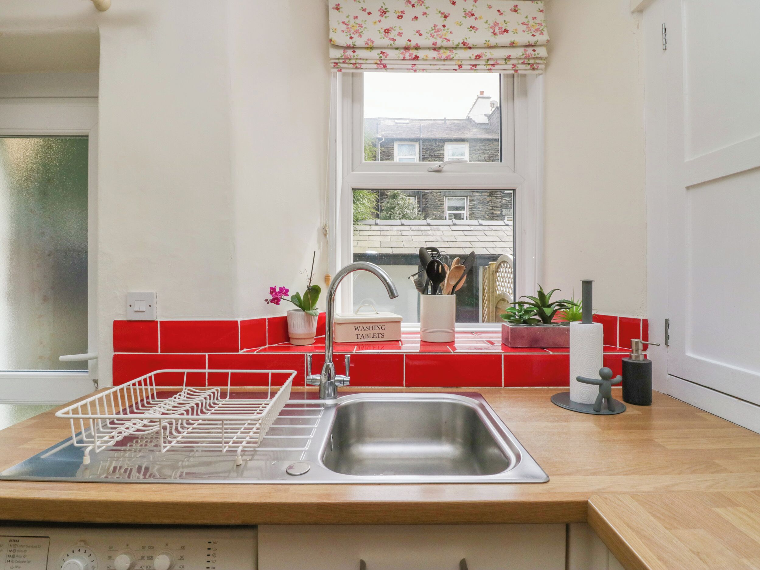 A kitchen with a stainless steel sink, red tiled backsplash, and a window with a view of buildings.
